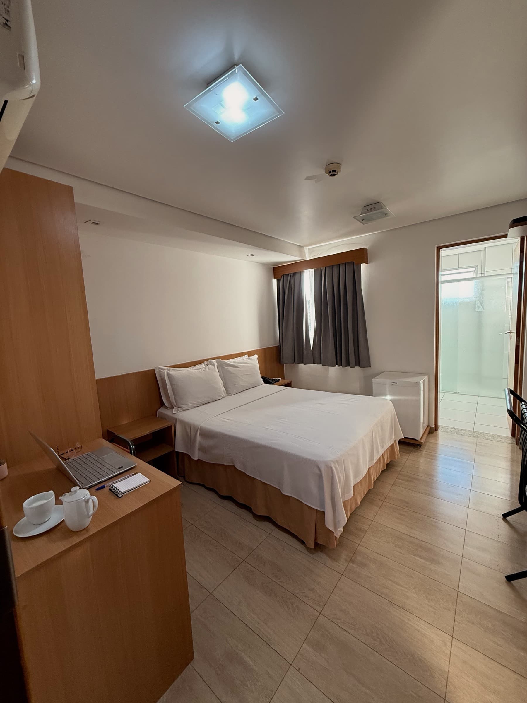 Quarto Standard com cama de casal, escrivaninha e banheiro ao fundo